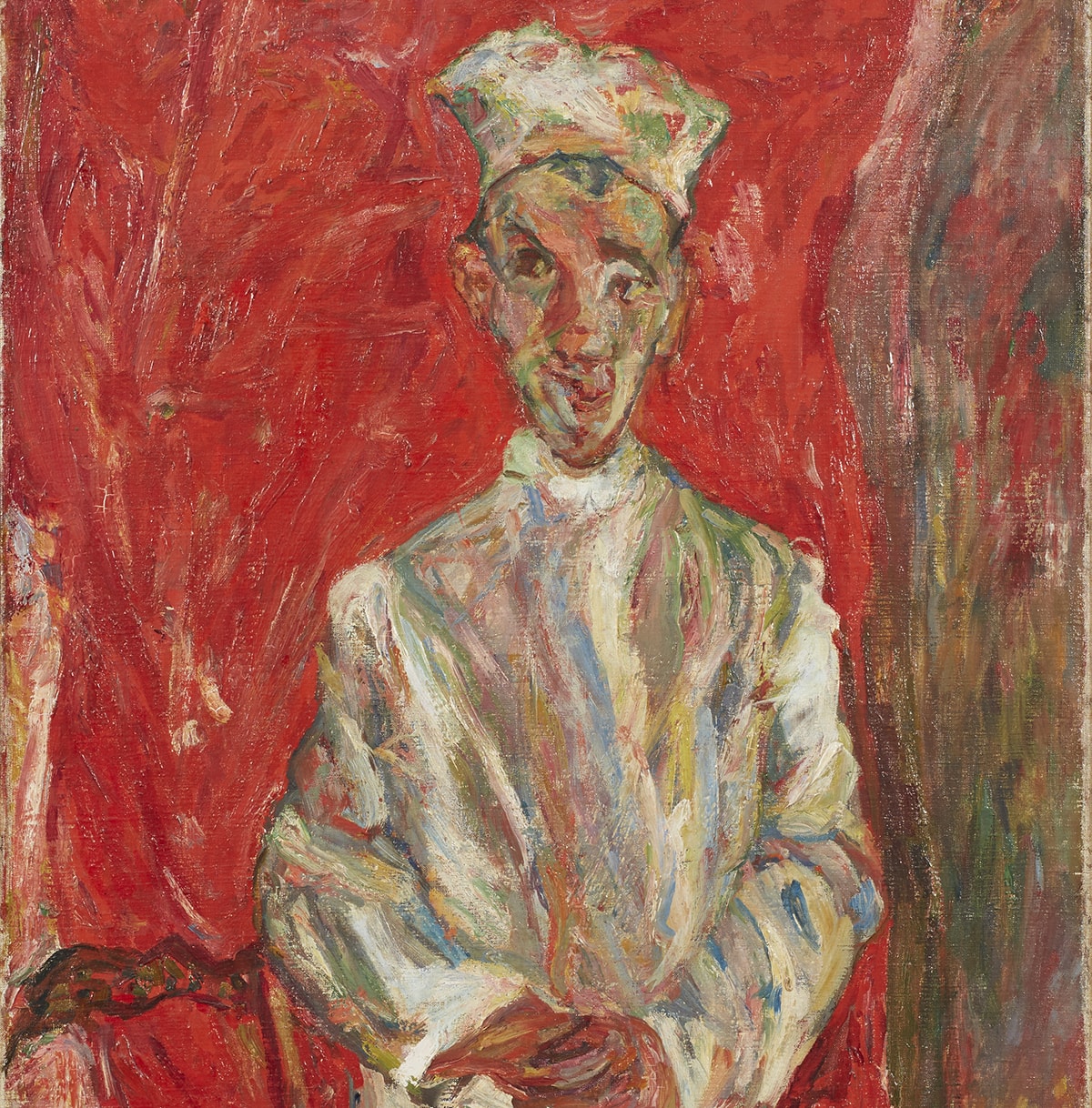 A vertical painting featuring a full-length male figure standing with his hands clasped in front. His left foot is placed in front of the other pointing to the right of the picture. He wears a cap atop a long face with a pointed chin. His ears protrude from either side of his head, bits of black hair poking out by his ears and at his forehead. Large dark eyes look off to the viewer’s left. He wears what appears to be a long-sleeve, high-collared white shirt. When examined more closely, the white shirt as well as his cap and shoes are made up of many colors in addition to white—grays, blues, green, yellows, tan, orange, and dashes of red applied in broad, rough brushstrokes. Similarly, his baggy, brownish pants are painted with strokes of brown, black, yellow, red, orange, and tan. To the left of the figure stands a brown chair with ornate slatted back. Behind the figure is a field of mottled red tones making up most of the width of the painting, suggesting a curtain. A narrow swath of reds, browns, yellows complete the right side of the painting running from top to bottom.