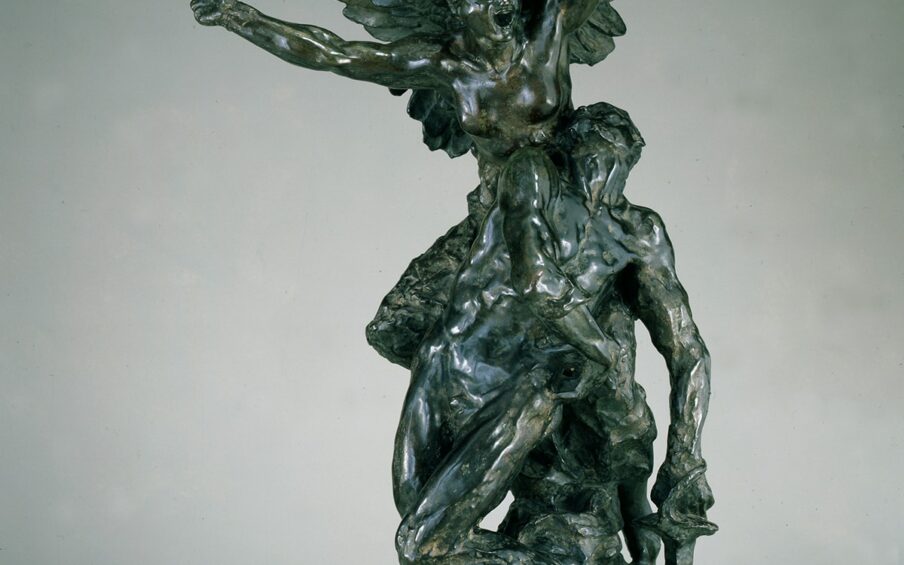 A photograph of a bronze sculpture showing two figures: the feminine presenting Spirit of Liberty and a masculine presenting combatant. The Liberty figure is positioned over the combatant. She is bare breasted with muscular arms raised in a V and fists tightly clenched. Her mouth is open wide as if shouting. She has a large pair of wings that rise behind her echoing the V of the arms. One wing is visibly broken and bent back on itself. The combatant is posed just beneath Liberty, and he looks up to her as if responding to her call. His nude body is set at a diagonal to Liberty’s with his head thrown back to the right, and his torso, hips and legs crossing diagonally to the left of Liberty. The leg at right is bent at the knee creating another angle. The arm at left lies across his body with his hand resting at right. His other arm is extended downward and he holds a sword that is inserted in the rocky base. He uses the sword to support his weak body as he tries to rise up toward Liberty. The sculpture is highly varied in its textured, displaying muscles, feathers, smooth skin and rock. The bronze is dark, almost black in some places with brownish highlights.