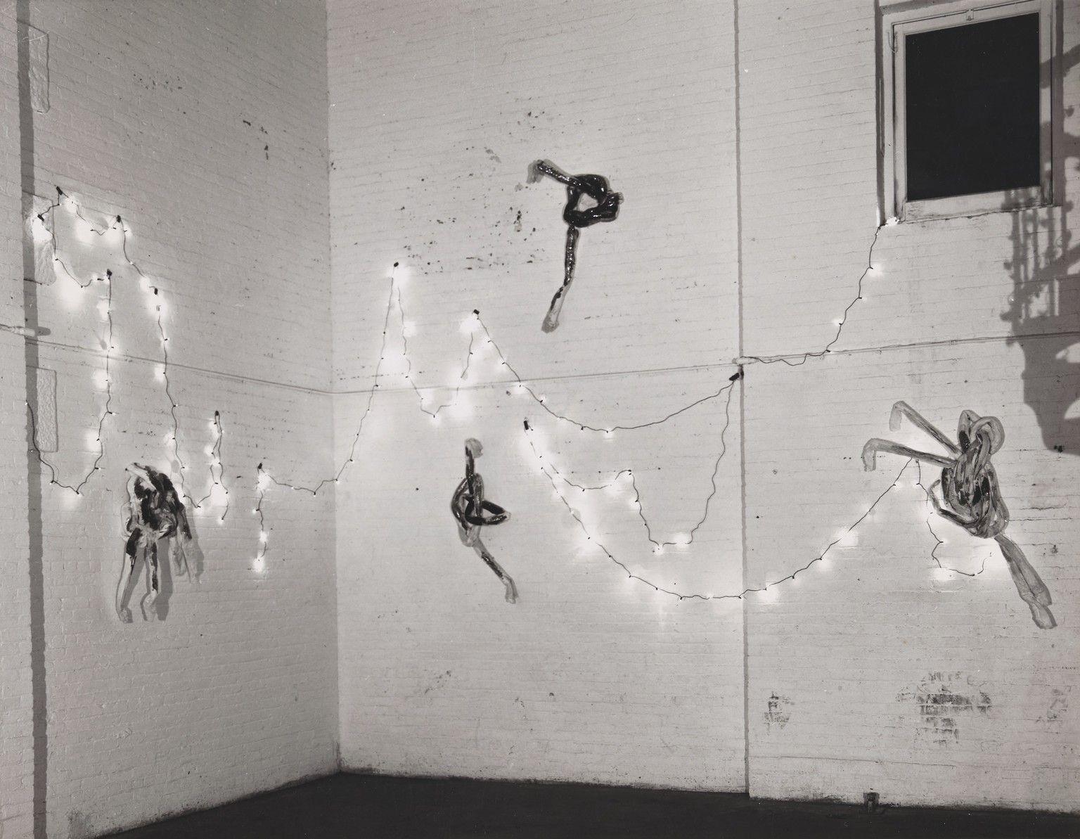 A black-and-white photo of a whitewashed brick interior with four “glitter knot” sculptures, hanging on the walls along with strands of small lights strung on the walls in a looping fashion.