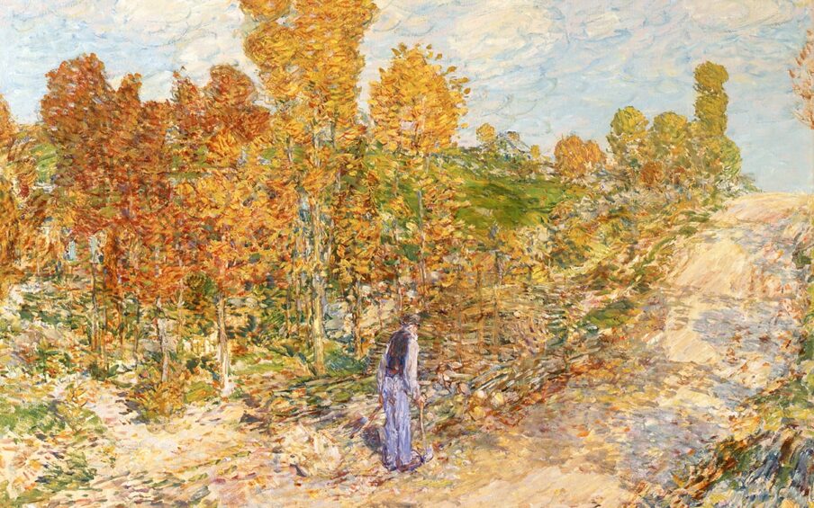 New England Road, Childe Hassam, 34 x 34 inches, oil on canvas. A square painting depicting a man walking along a rural road in autumn. The road is positioned diagonally across the painting starting at the lower left corner where it is broad and wide and continues to center right where it narrows slightly, ending at the horizon line a third of the way from the top. Shadows from nearby trees fall across the road’s pale, tan surface. The top third of the painting is a blue sky with drifting, billowy clouds in pale, watery blues and whites. The center area of the work features a stand of trees with leaves of rusty red and yellow amid green grass, shrubbery, and fallen leaves. At center, a man stands with his back turned wearing a light-colored shirt, a dark vest, light blue trousers and a hat. He carries an ax as though he has been chopping wood at the roadside. Paint is applied with small brush strokes and colors are layered creating a soft effect without hard edges.