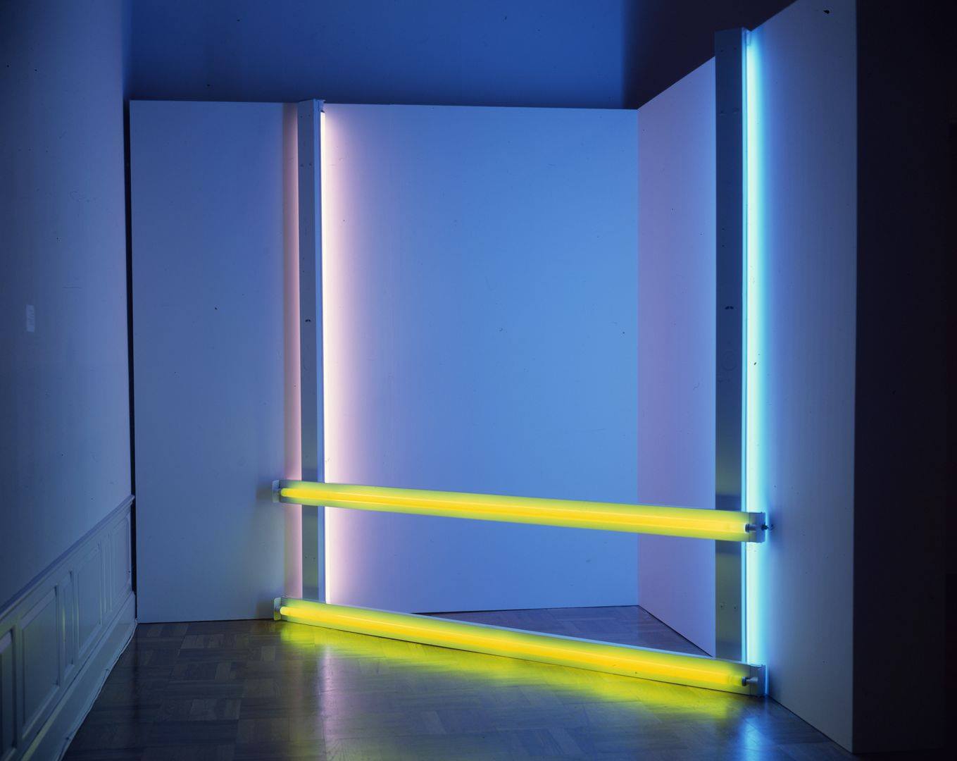 Untitled (to Donna) 2, 96 ¼ x 96, fluorescent light. An installation of fluorescent lights positioned in a corner consisting of two bright yellow lights running horizontally at floor and knee level and two fluorescent lights running horizontally at each end with the light component facing the wall. The horizontal lights are bright blue at the right and mauve at the left. All four lights cast their colors on the corner walls and floor.