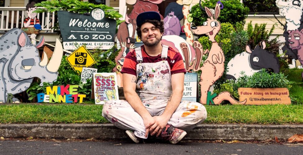 Artist Mike Bennett sitting on the curb in front of a house with his artwork on the lawn