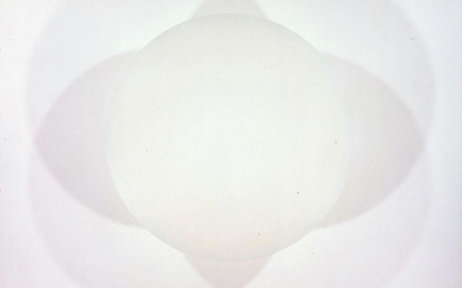 Untitled, Robert Irwin, 48 inches in diameter, spray enamel on aluminum. A photo of an ivory disc casting shadows on the wall behind it. Light shines from below causing four overlapping shadows to appear around the disc. The shadows are pale gray and deepen slightly when overlapped. The shadows and disc create one large intricate shape when looked at together or five separate simple shapes when viewed individually.