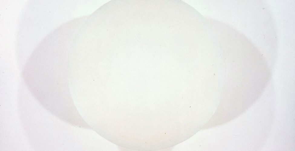 Untitled, Robert Irwin, 48 inches in diameter, spray enamel on aluminum. A photo of an ivory disc casting shadows on the wall behind it. Light shines from below causing four overlapping shadows to appear around the disc. The shadows are pale gray and deepen slightly when overlapped. The shadows and disc create one large intricate shape when looked at together or five separate simple shapes when viewed individually.