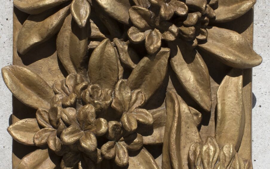Image description: “Rhododendrons.” Marie Louise Feldenheimer. 1933. Bronze. 19 1/2 x 15 1/2 x 6 inches. A rectangular, monochromatic, bronze plaque with four rhododendron flowers in relief. A tight bud appears in the upper left corner, fringed with leaves and pointing toward the corner. Two, fully open flower clusters form a diagonal from the lower left corner to the upper right corner, each framed by large, smooth leaves. In the lower right corner, a partially open flower is seen from the side, facing toward the edge, the edges of its leaves curve gently. Strong sunlight on the relief creates deep shadows and glossy areas, suggesting the shine of actual rhododendron leaves.