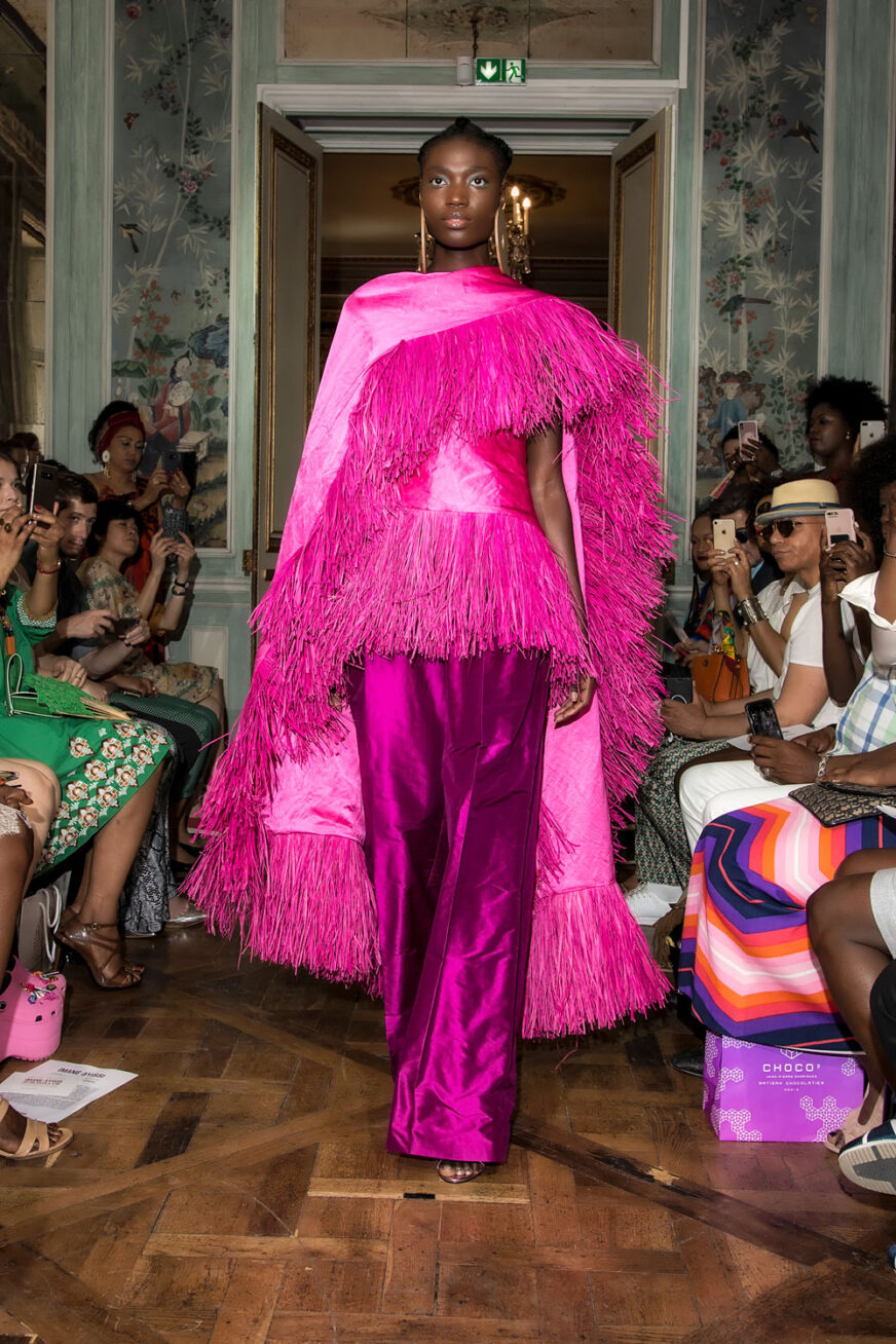 Photograph of a black model walking on a catwalk in a bright pink outfit