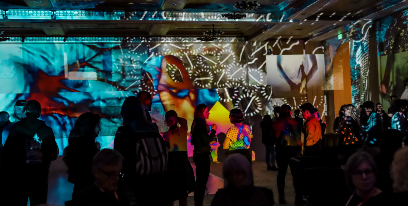 Photograph of a about 20 people at party in a dark room with different patterned light reflections on the walls