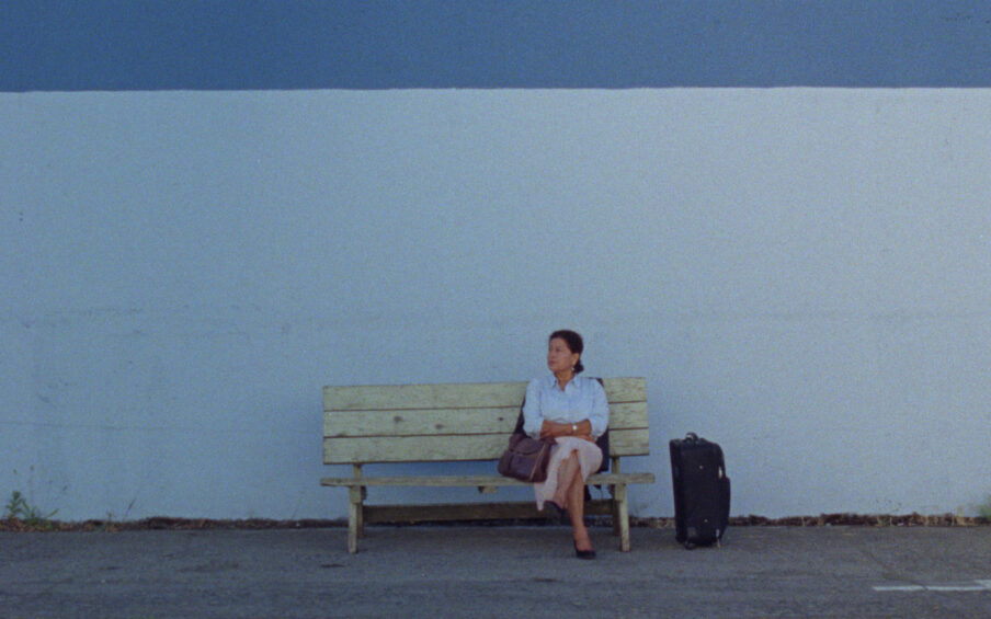 A person sitting on a bench with luggage on the ground next to them