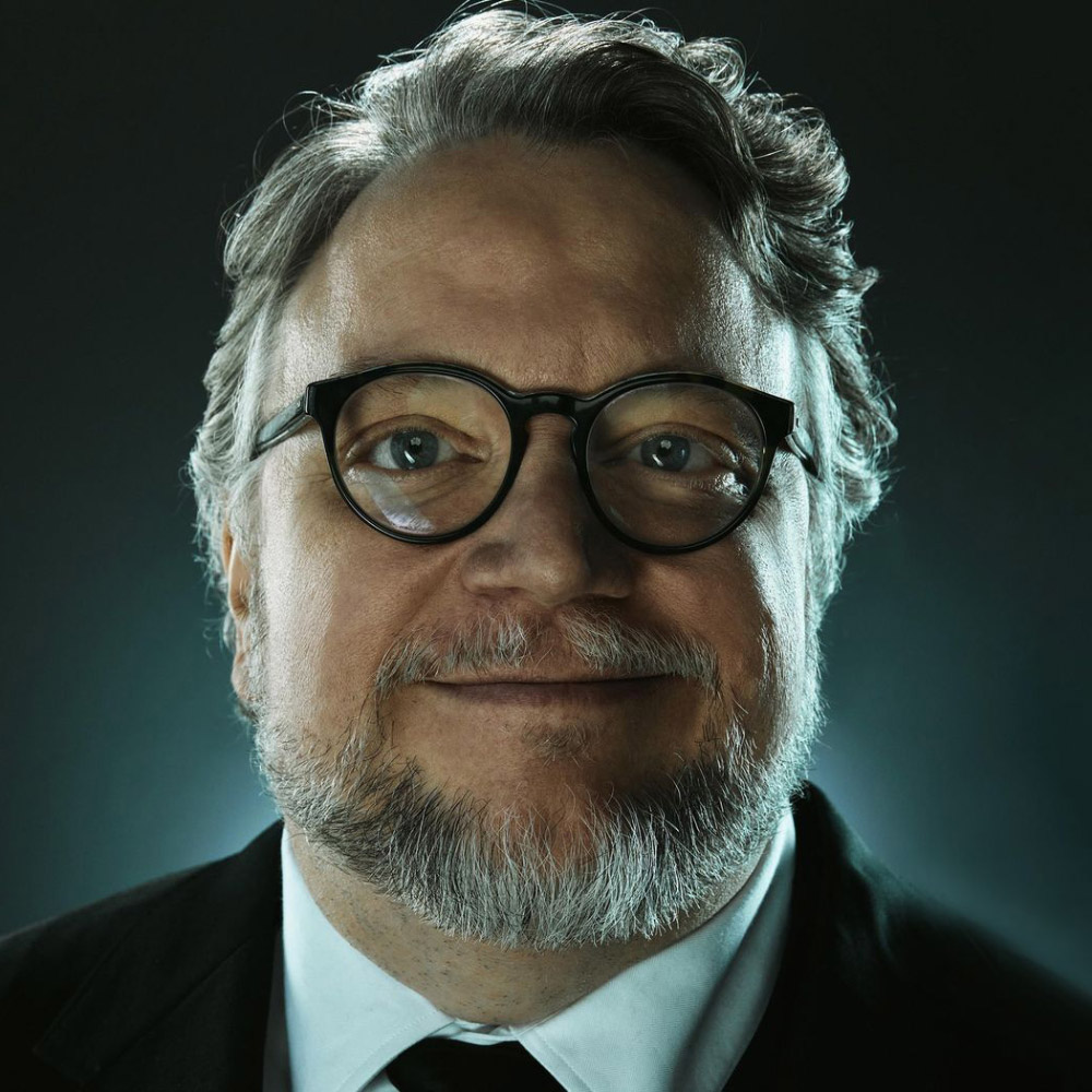 Close up portrait of Guillermo del Toro wearing glasses, a white shirt and black blazer