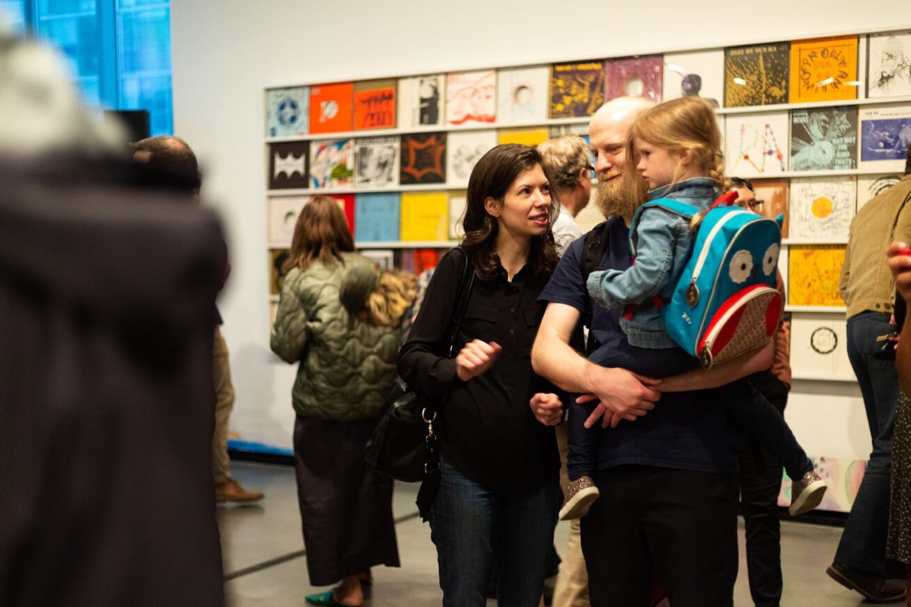 A family with a young child standing with other in a gallery looking at art