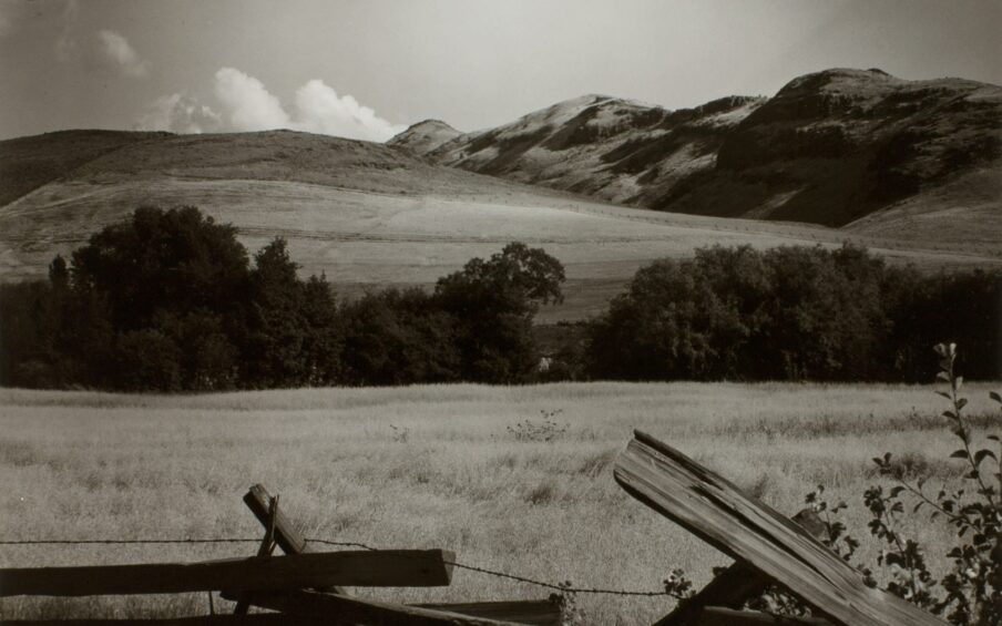 Black and white photograph of open hills with a broken fence in the foreground.