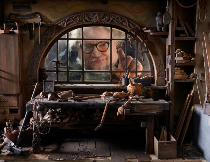 Photo of a man looking through a window towards a Pinocchio puppet laying on a table