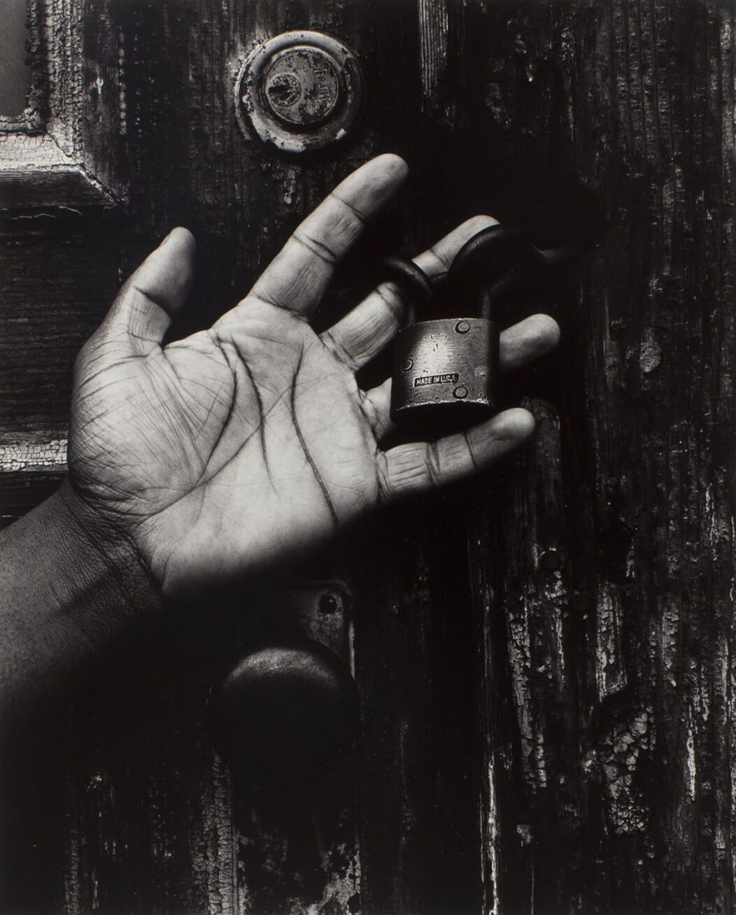 Black and white photo of a hand holding a lock in front of a wooden door