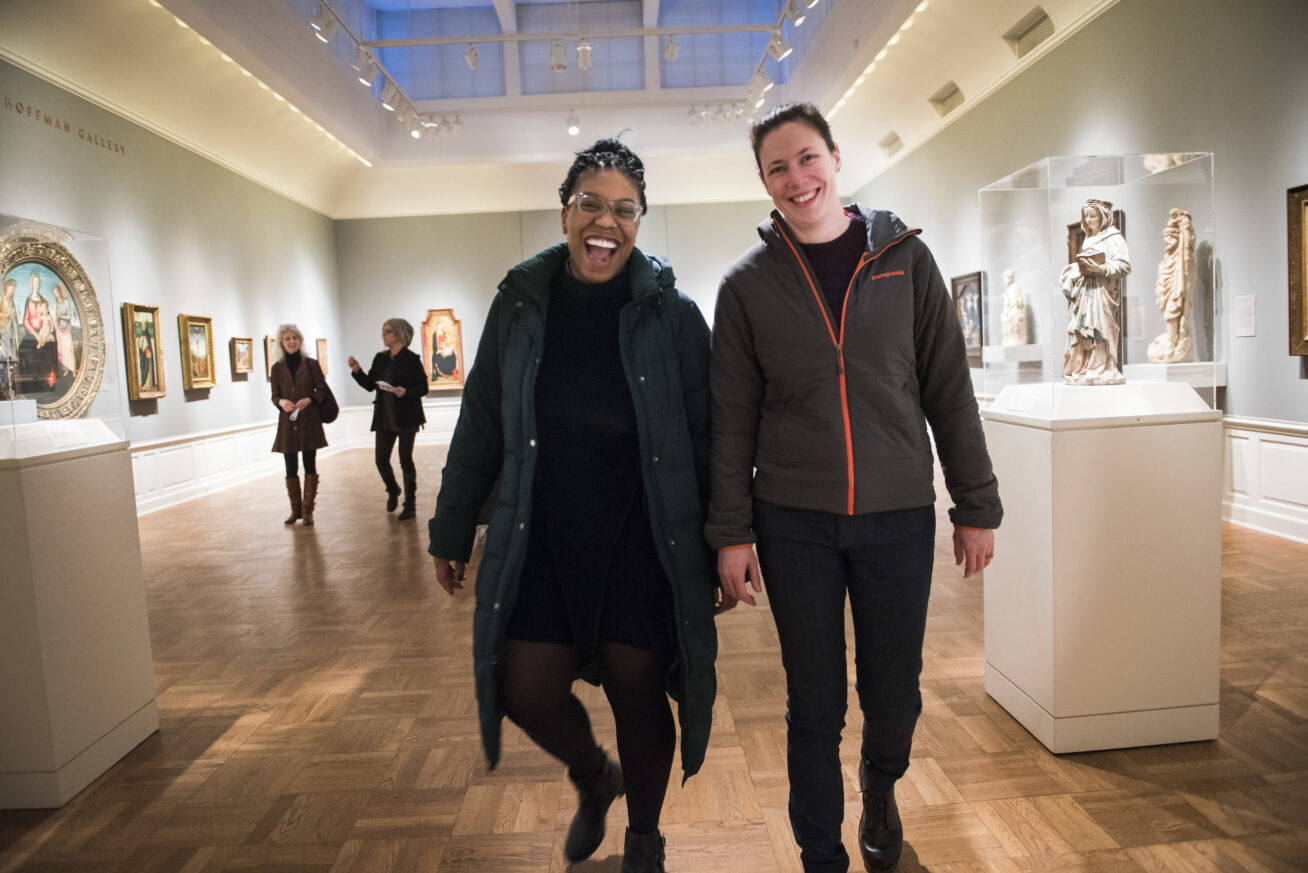 Two people smiling and walking toward the camera in an art gallery.