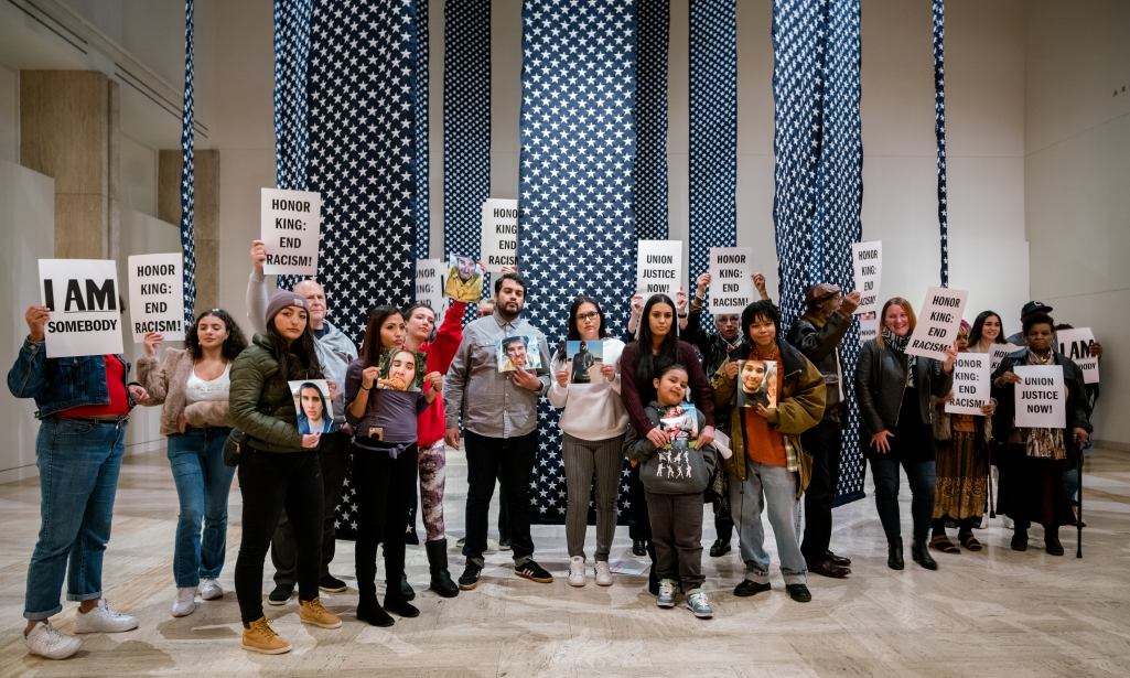 Group of people at the Hank Willis Thomas exhibition holding up signs like "Honor King: End Racism" and "I am Som