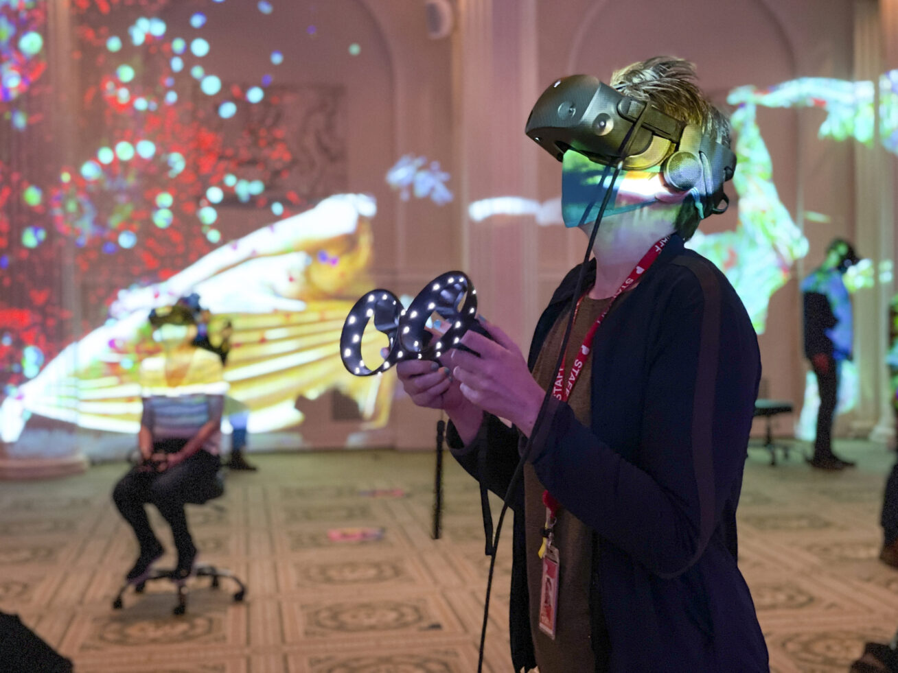 Photo of a person in a colorfully lit room using a VR headset and handset.