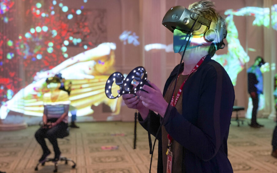 Photo of a person in a colorfully lit room using a VR headset and handset.