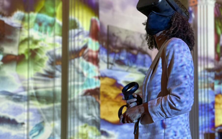 Photo of someone wearing a VR headset in a room with colorful projections on the walls.