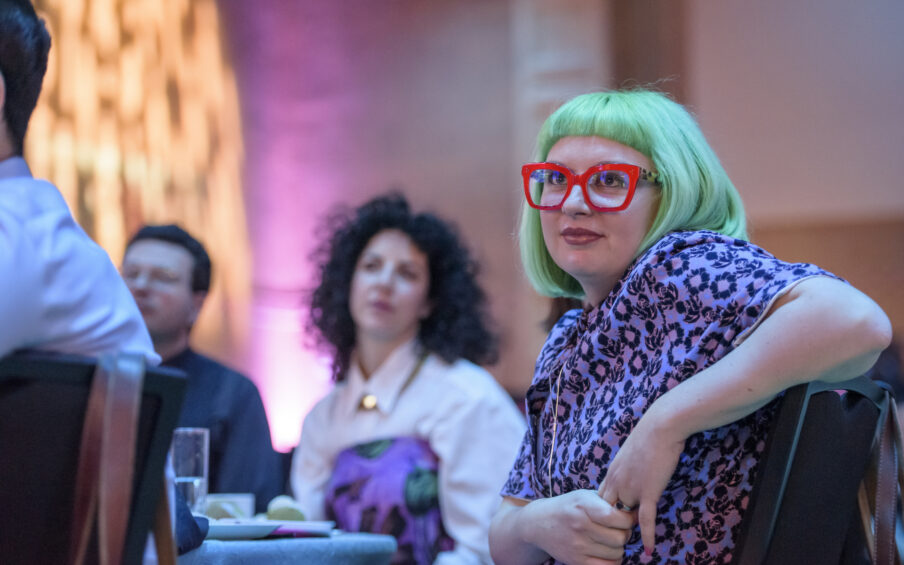 Photo of woman in the foreground with green hair and pink glasses.