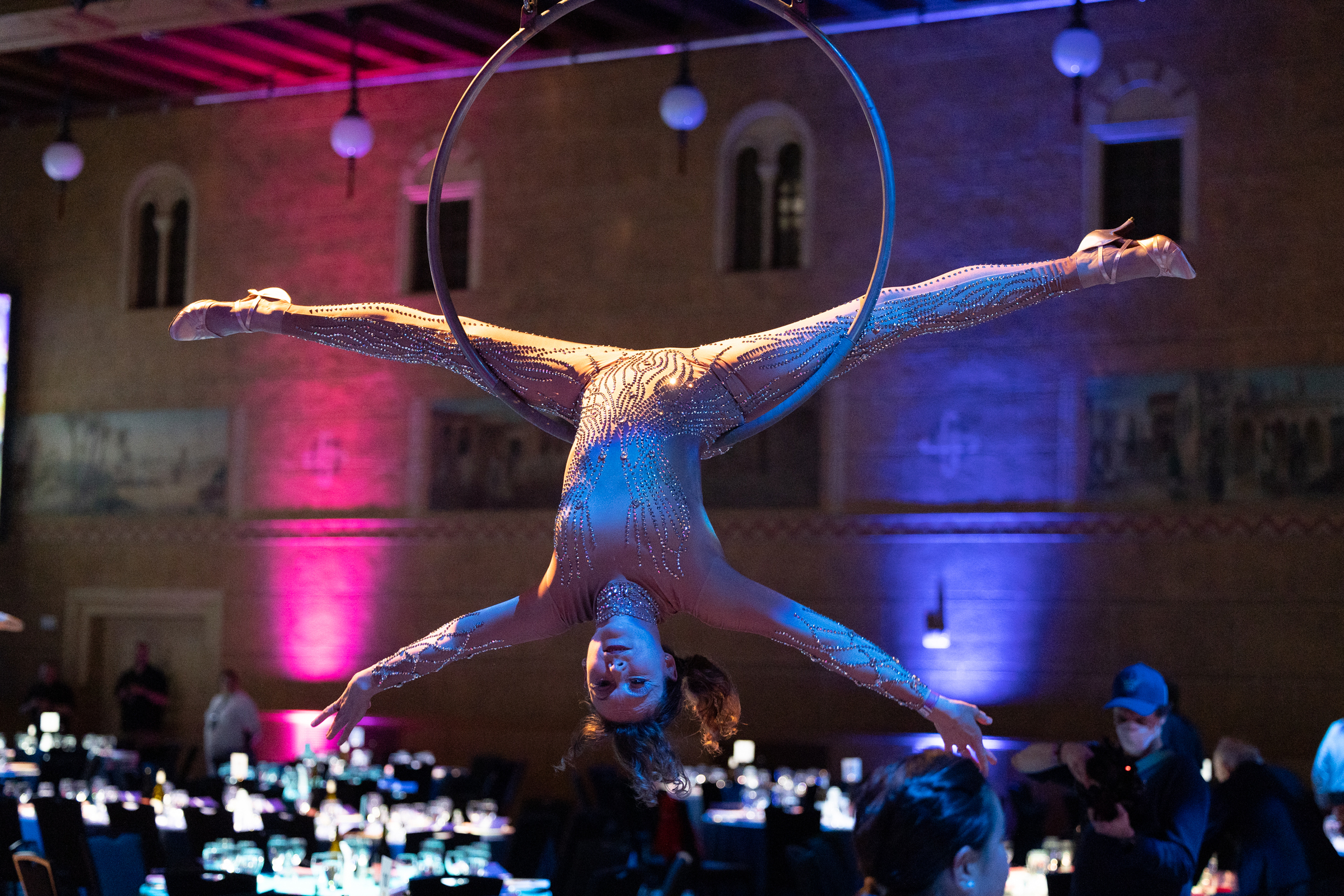 Aerial acrobat hanging upside down in a ring inside of a ballroom.