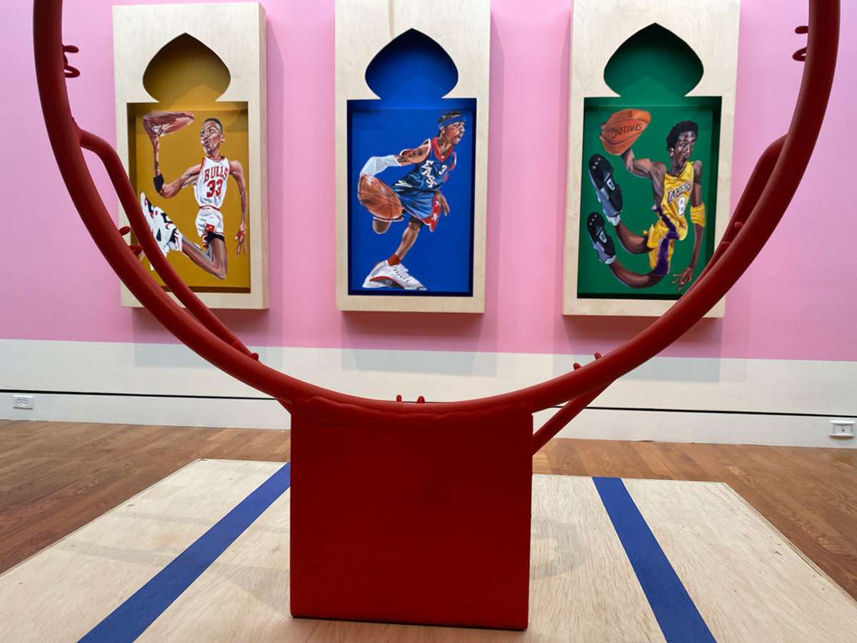 Photo of a gallery with a basketball hoop and three paintings of basketball players in frames shaped like Moroccan architecture