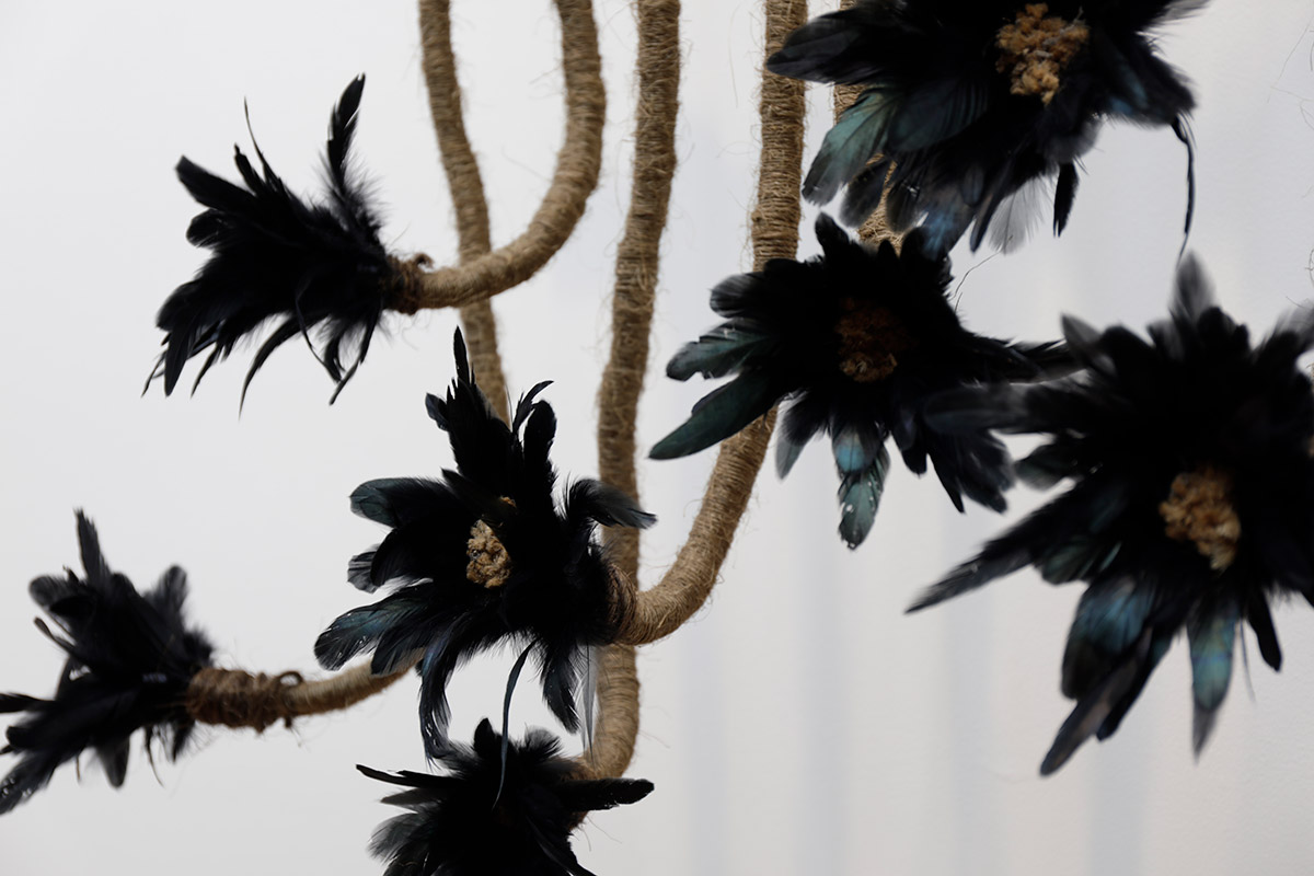 Sculpture of flowers made from black feathers and a light brown twine wrapped around the stems