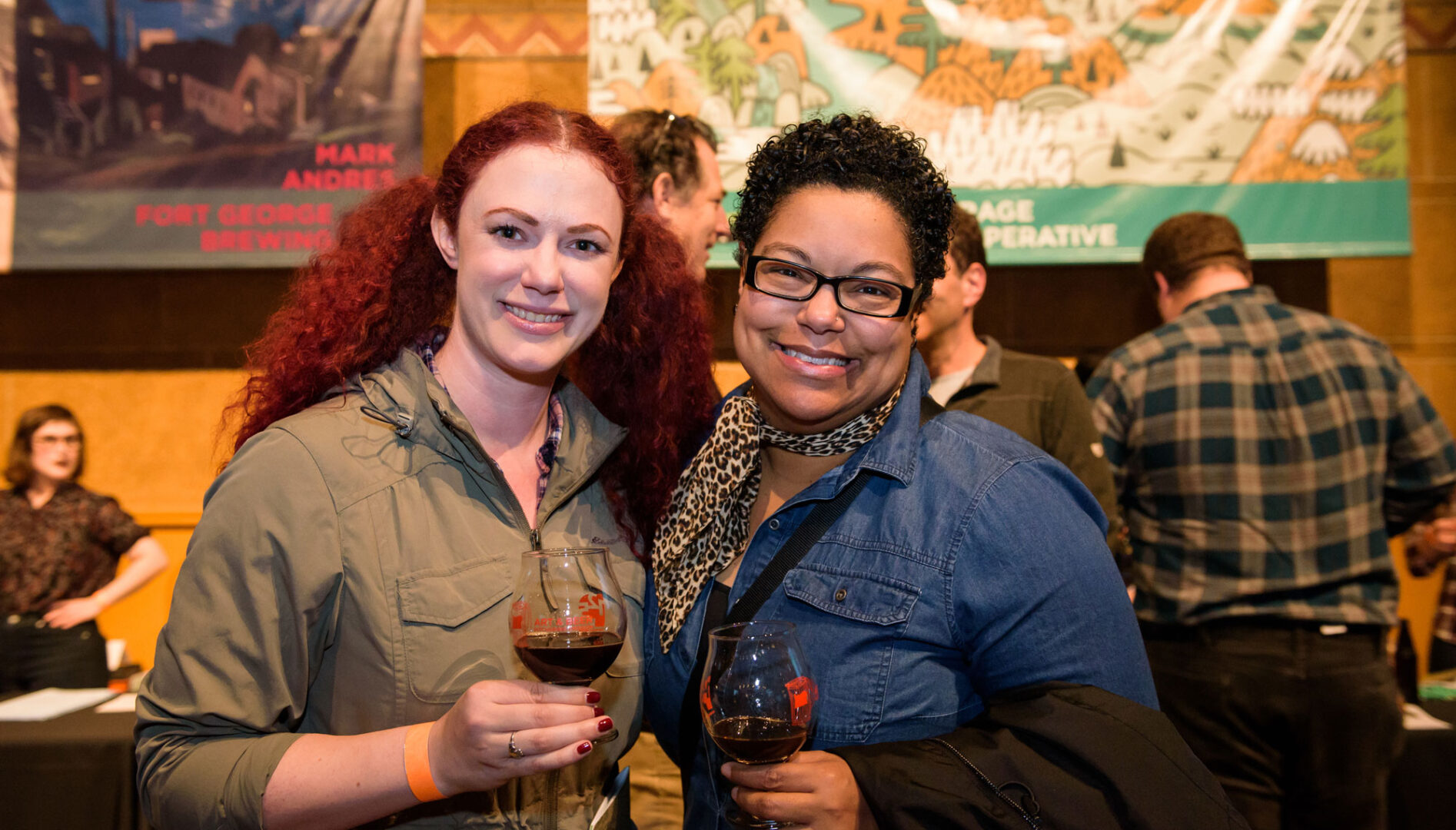 A woman with long red hair and a woman with short brown hair smiling at the camera and holding glasses of beer