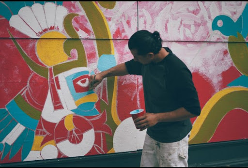 A man turned away from the camera panting a mural on a wall.