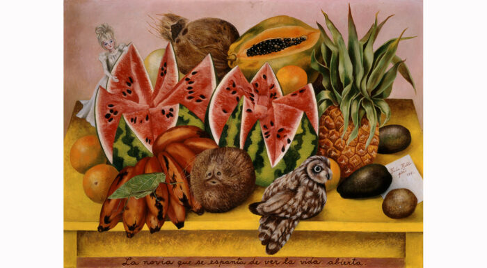 Frida Kahlo painting of watermelon, papaya, coconut, plantain, pineapple, avocado, and oranges, with a blonde doll in the back left corner and a small owl in the front right corner.