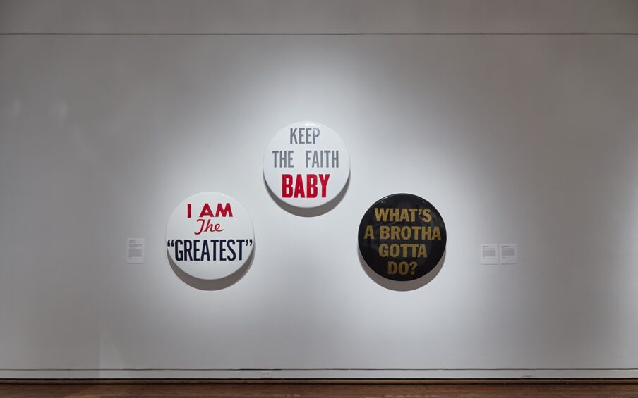 Gallery wall with three Hank Willis Thomas round artworks saying "I am the Greatest", "Keep the Faith Baby", and "What's a Brotha Gotta Do?"
