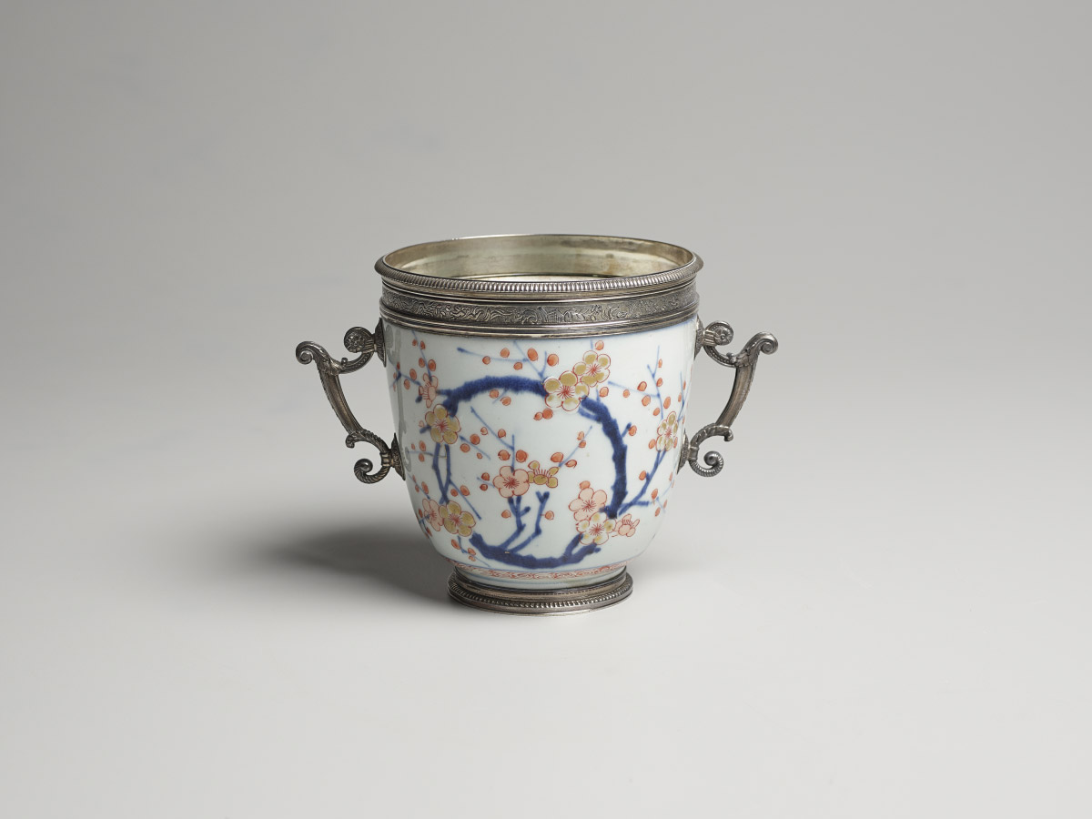 A small porcelain bowl decorated with cherry blossoms, with silver handles on both sides and a silver rim