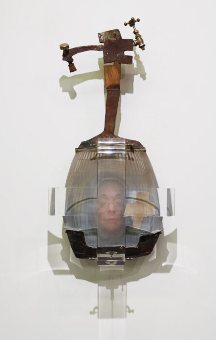 Sculpture made of metal, glass, and plastic with the image of a woman's face with closed eyes in the middle