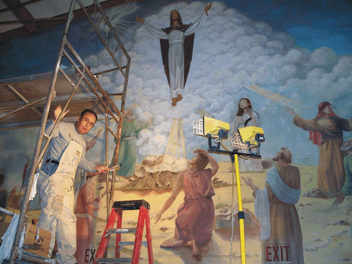 A mural of Jesus ascending to heaven. To the lefthand side, a man in overalls is standing on scaffolding next to a ladder.