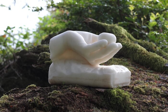 Sculpture of a hand holding a plum resting on a log with trees surrounding