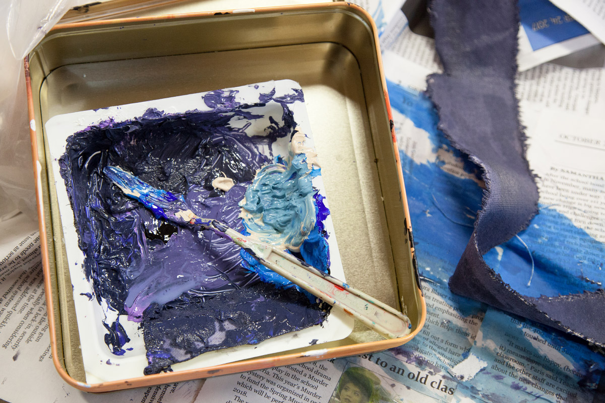 A square tin with tray full of blue paint in it. A paint knife sits in the paint.
