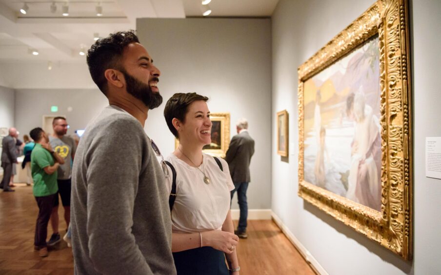 Two people viewing a framed painting in a gallery.