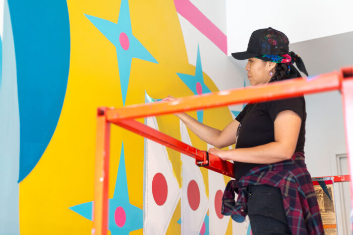 Artist Lynnette Haozous working on the mural “Into the Sun,” 2021