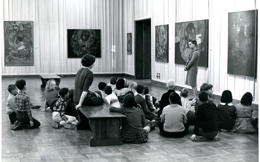 Historic, black and white photo of children sitting on the floor in an art gallery.