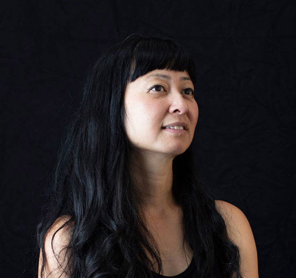 Portrait of a woman with long black hair looking off to the side against a black background