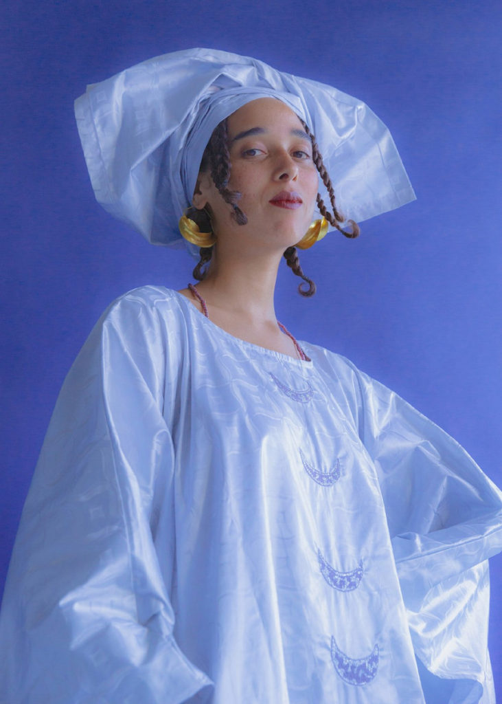 Portrait of a woman with a satin light blue dress and headwrap against a purple background