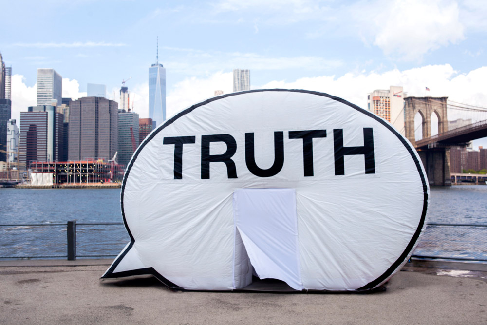 A photo of a life-size speech bubble that says "TRUTH" in front of the Willamette River and Portland skyline