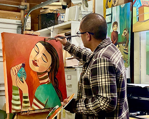 A man facing away from the camera painting  an artwork of a woman with her eyes closed and her head tilted upward.