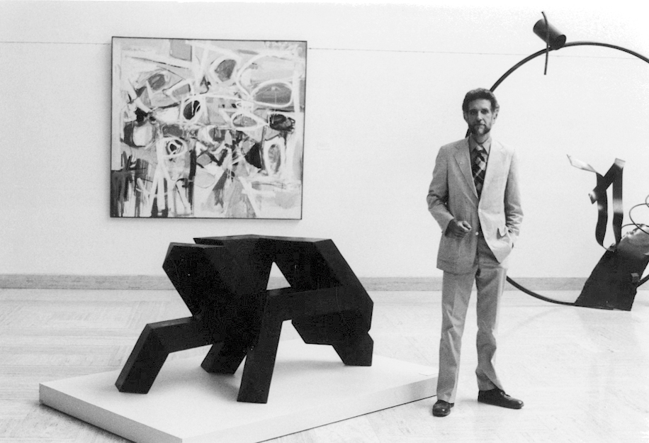 Black and white photo of a man in a suit standing in an art gallery.