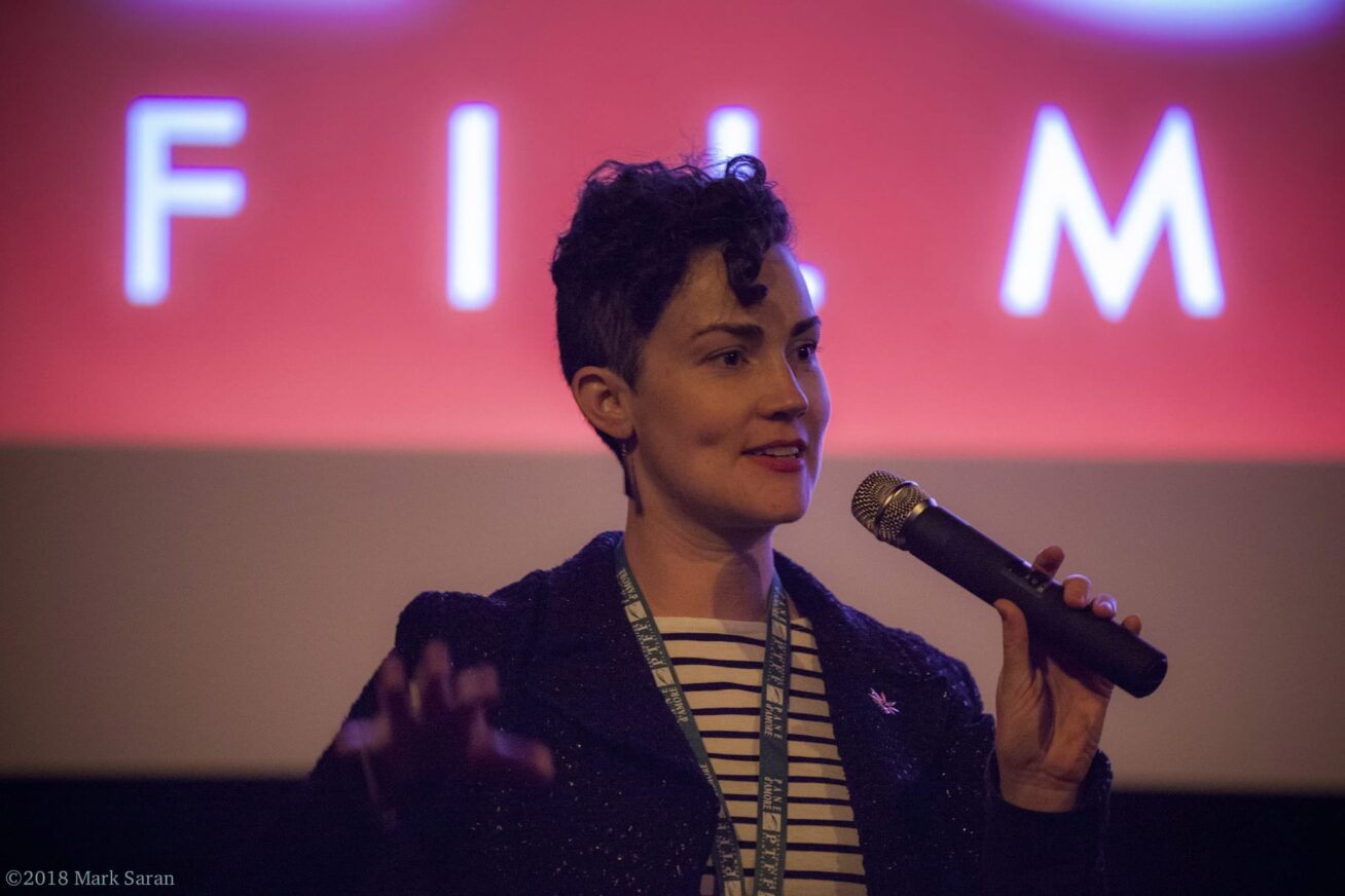 A person holding a microphone with the word "film" projected on a screen behind them.