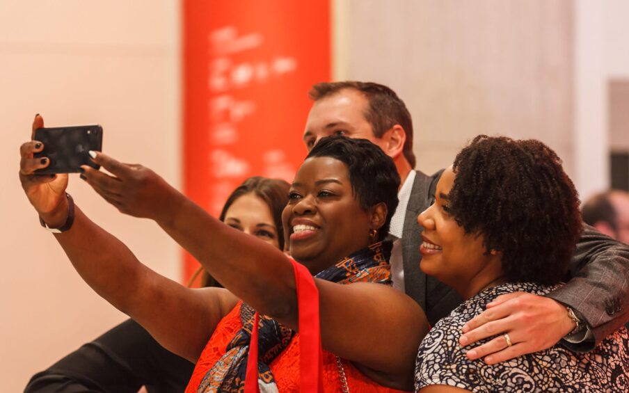 A group of four people huddled together taking a selfie in a gallery space.