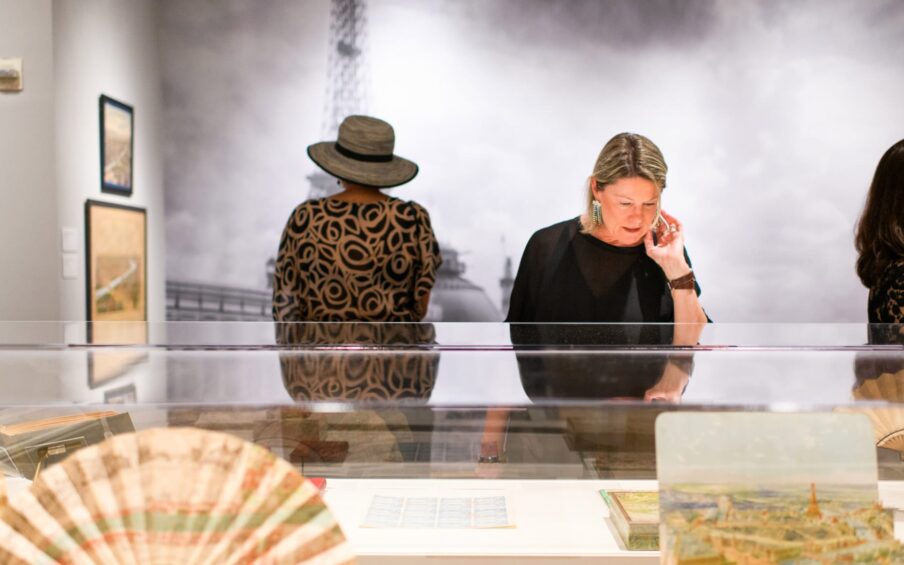 One person examining artwork displayed in a glass case and another person viewing artwork on a wall.