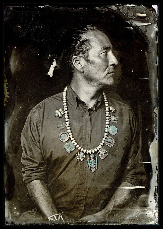 Sepia toned photograph of a Native American man in a silver and turquoise necklace, looking to the side.