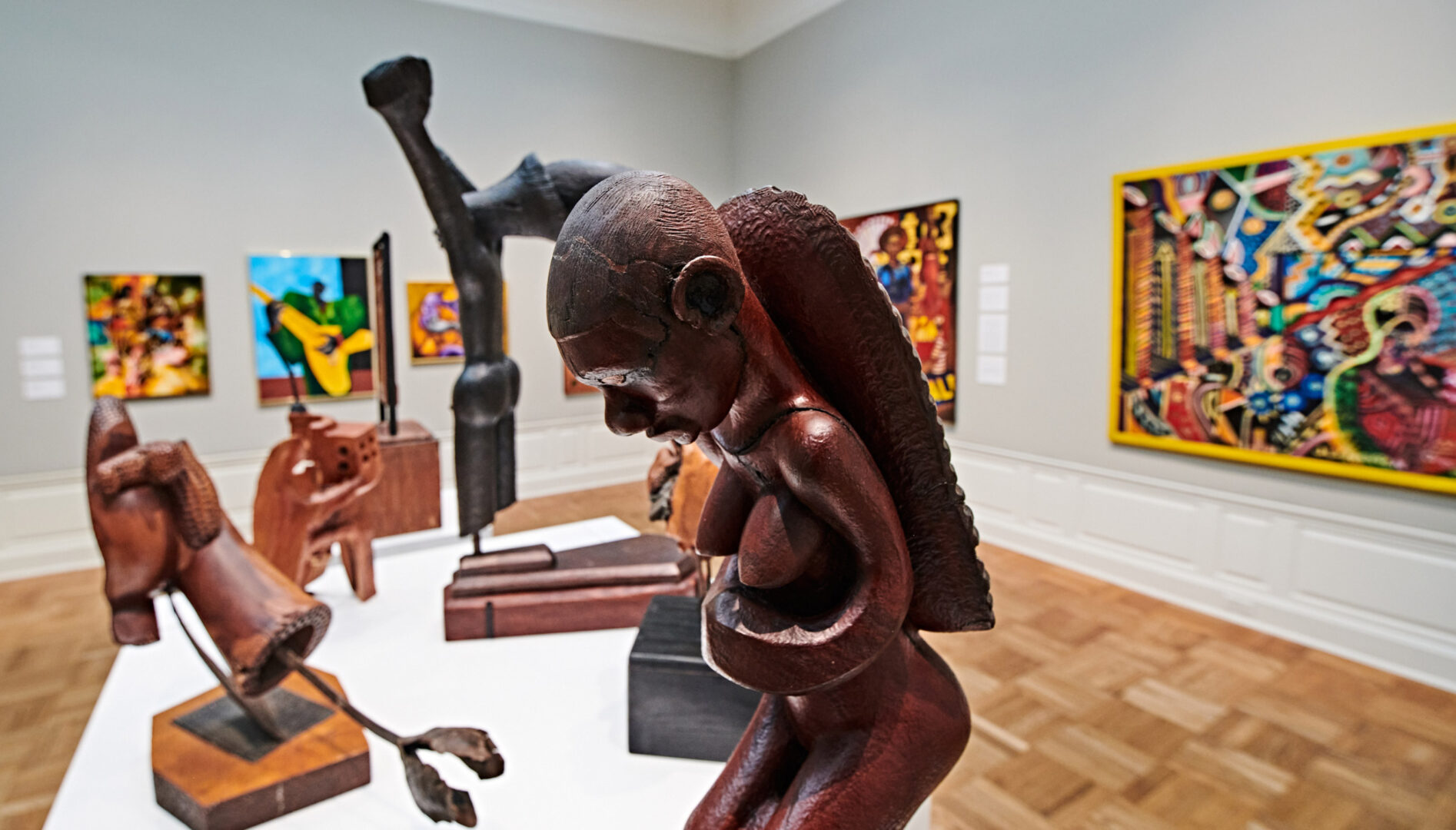 A gallery view with sculptures in the foreground and paintings in the background.