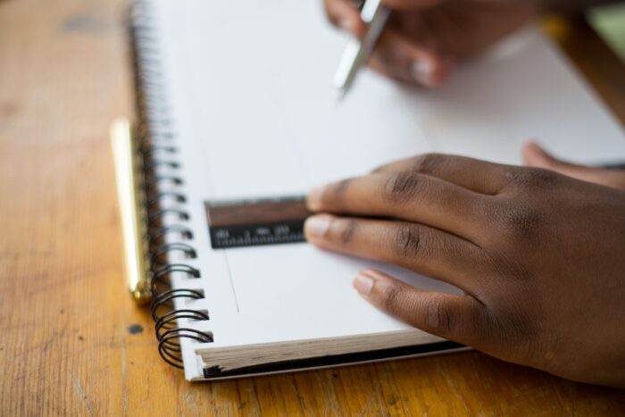 Photo of hands holding a pen and a metal ruler on top of a notebook