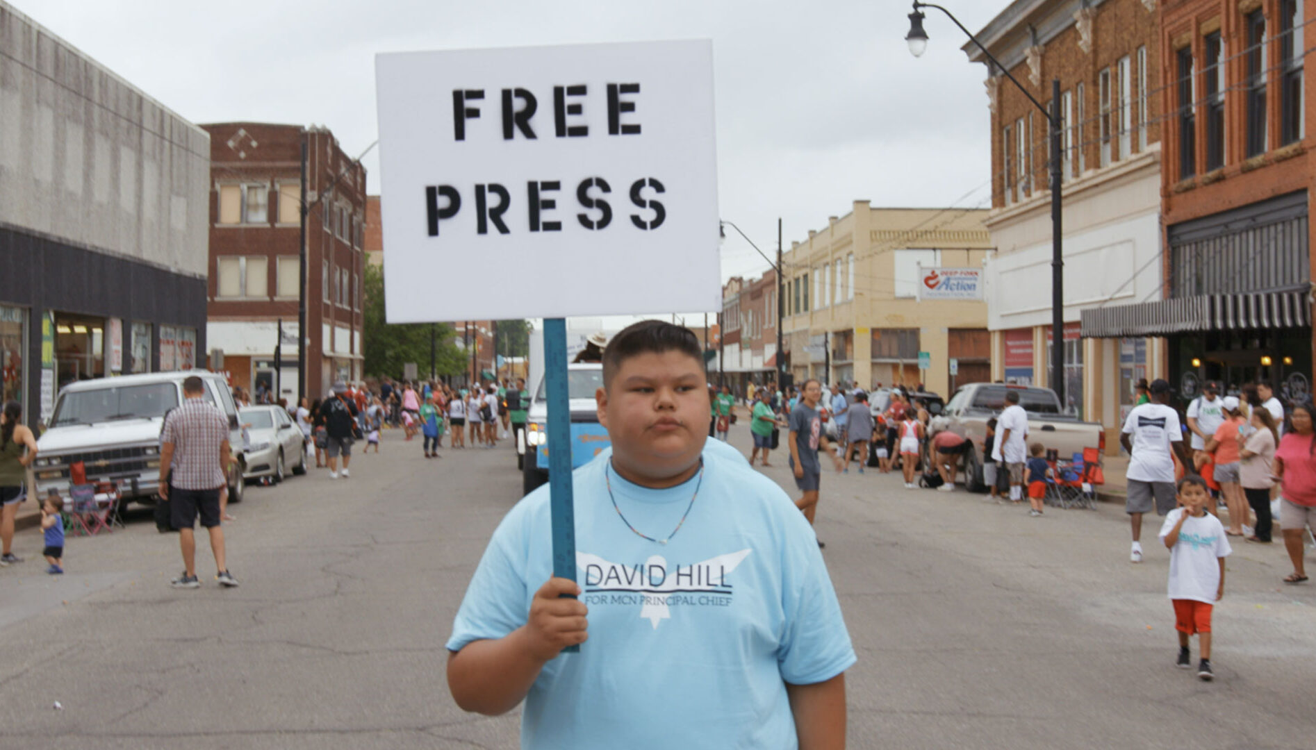 Photo of a man in a blue shirt standing on a street holding a "Free Press" protest sign